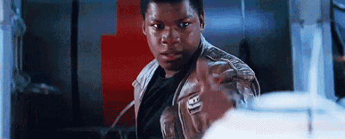 a man in a leather jacket is standing in a room and pointing at the camera .
