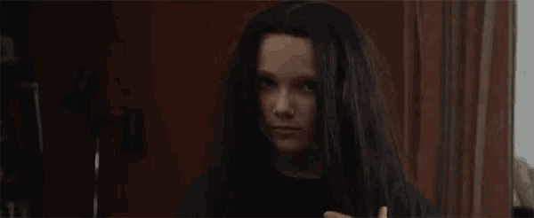 a young girl with long black hair is standing in front of a mirror holding her hair .