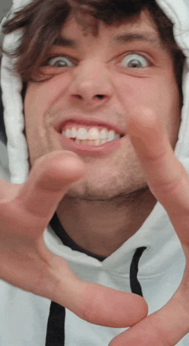 a man in a white hoodie is making a funny face with his hands