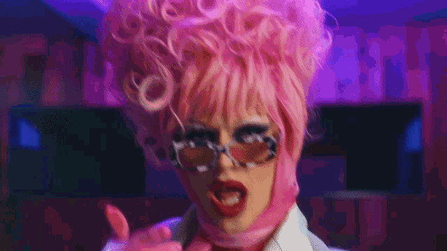 a woman in a pink wig and sunglasses is making a funny face while holding a cup .