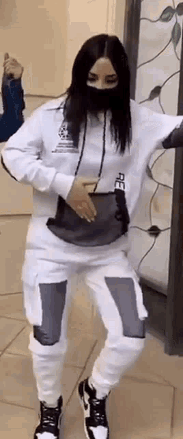 a woman wearing a black mask and a white hoodie is dancing .