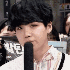 a young man is talking into a microphone while standing in front of a crowd of people .
