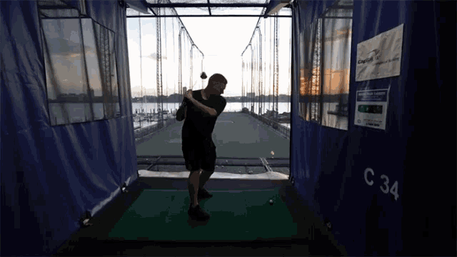 a man is swinging a golf club in a cage with a sign that says capital one