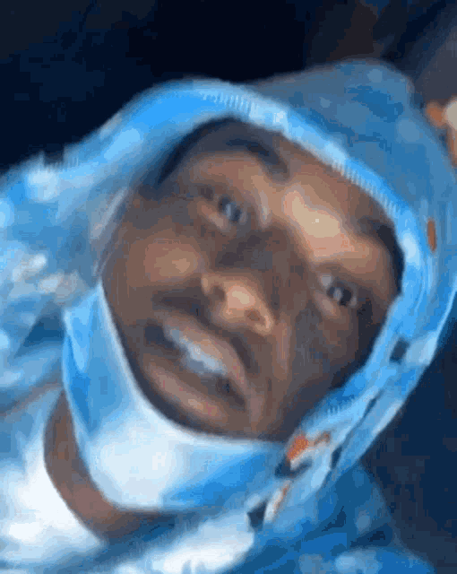 a close up of a man wearing a blue hoodie and a mask on his face .