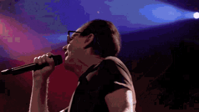 a man with glasses is singing into a microphone on a stage