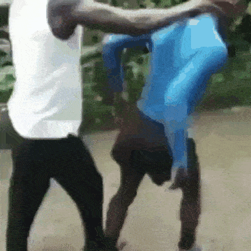a man in a white shirt is standing next to a man in a blue shirt who is doing a handstand .