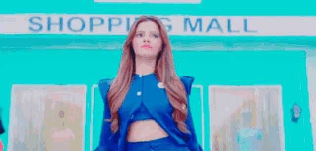 a woman in a blue dress is standing in front of a shopping mall .