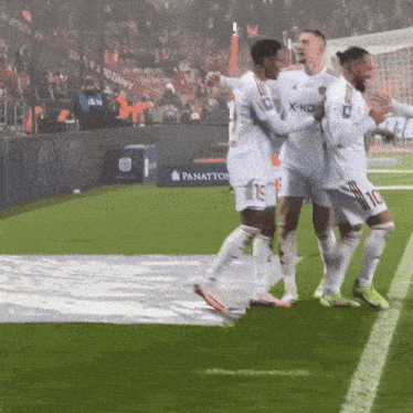 a group of soccer players are celebrating a goal on a field with a panation sign in the background