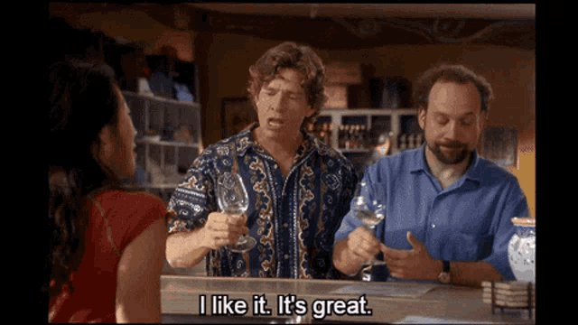 a man in a blue shirt is holding a wine glass and says i like it it 's great