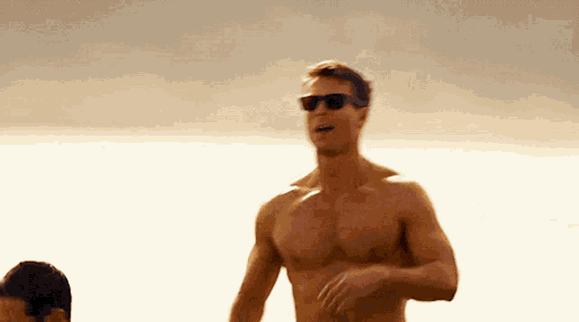 a shirtless man wearing sunglasses is standing on a beach