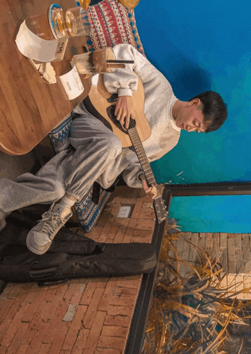 a man sits at a table playing a guitar with a cup of coffee and a bottle of coca cola on the table