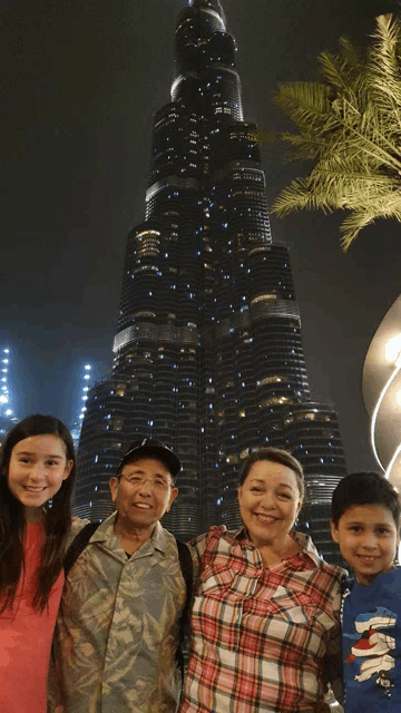 a family posing for a picture in front of the world 's tallest building at night