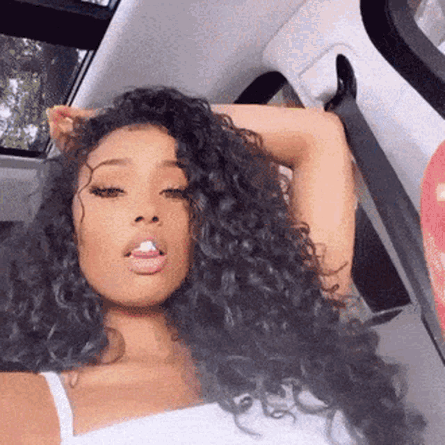 a woman with curly hair is sitting in the back seat of a car with her hand on her head .