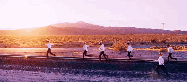 a group of people are running on train tracks in a desert