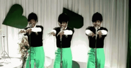 three men in green pants are standing in front of microphones on a stage .