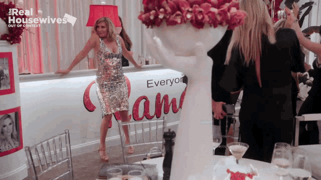 a woman in a sequined dress is standing in front of a bar that says " everyone "