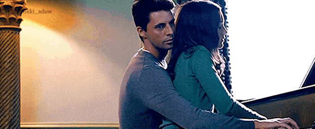 a man and woman are hugging while playing a piano .