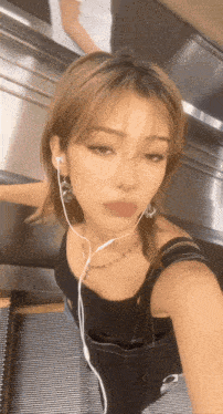 a woman wearing ear buds and a black tank top takes a selfie