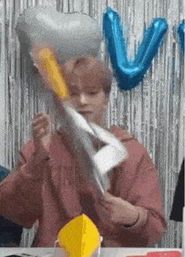 a man is sitting at a table with balloons in the background and holding a piece of paper .