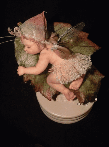 a figurine of a baby fairy is sleeping on a green leaf