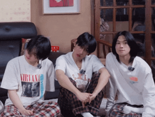 three young men are sitting in a living room with one wearing a nirvana t-shirt
