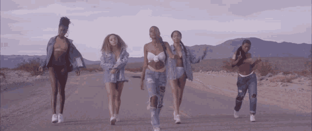 a group of young women are walking down a dirt road