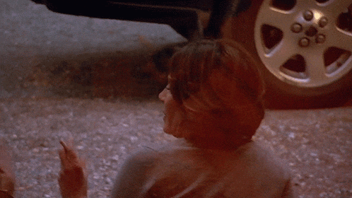 a woman smoking a cigarette in front of a silver car wheel