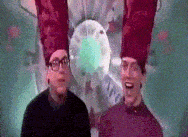 two men wearing red hats and glasses are standing next to each other in front of a green light .