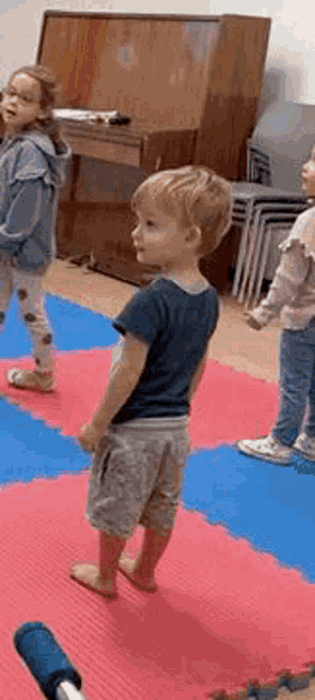 a group of young children are standing on a red and blue mat in a room .