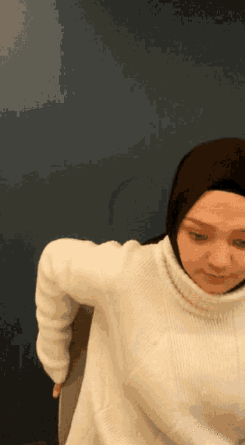 a woman wearing a hijab and a white sweater is standing in front of a blue wall