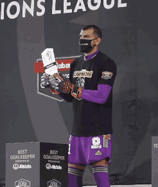a man wearing a mask holds a trophy in front of a sign that says " best goalkeeper "