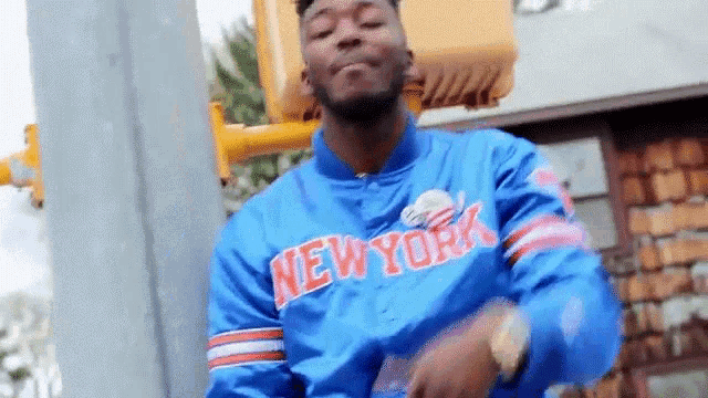 a man in a blue jacket with the word new york on it is standing in front of a traffic light .