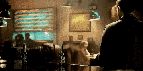 a man is standing behind a bar in a restaurant with bottles of beer .