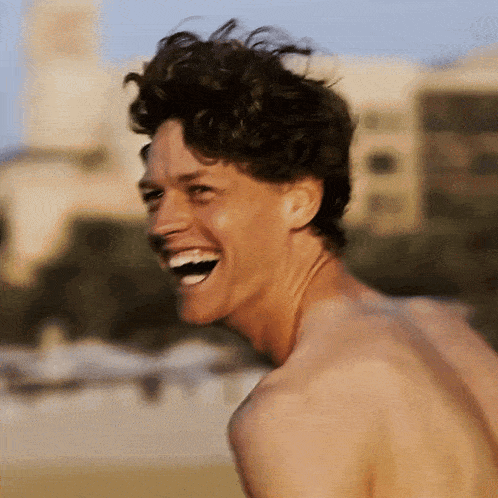 a shirtless man laughs with his mouth open