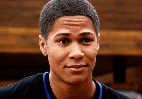 a young man wearing a black shirt with a blue ribbon around his neck looks at the camera
