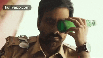 a man in a police uniform is holding a green bottle in front of his face .