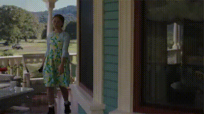 a woman in a dress is standing on a porch next to a house .