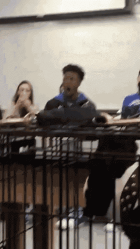 a group of people are sitting at desks in a classroom and one of them is wearing a blue shirt that says washington