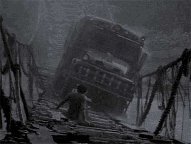 a black and white photo of a man looking at a truck that has crashed into a bridge