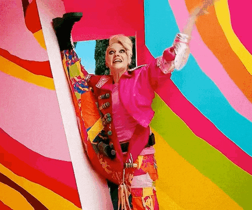 a woman in a pink jacket is doing a split while standing in front of a colorful wall .