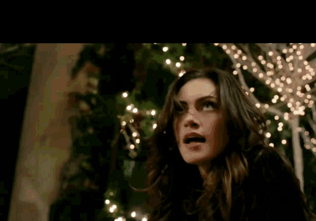 a woman stands in front of a tree with christmas lights