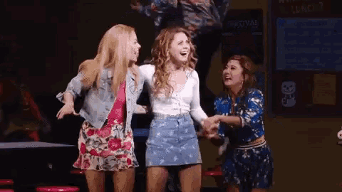 three women are standing next to each other on a stage holding hands and laughing .