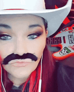 a woman wearing a cowboy hat and a fake mustache is standing next to a guitar that says nin