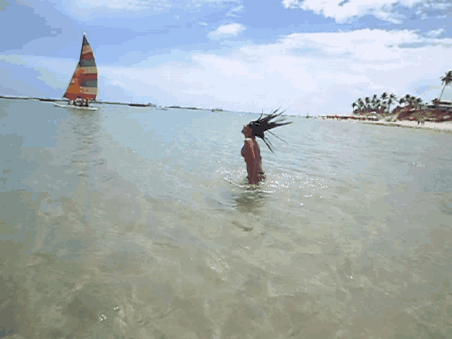 a woman is swimming in the ocean near a sailboat