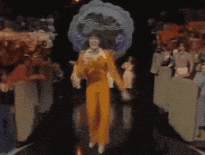 a woman in a yellow jumpsuit is dancing on a stage in front of a crowd