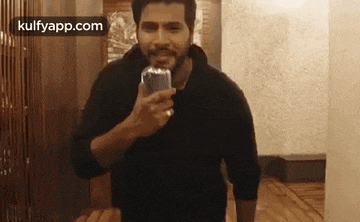 a man is standing in a room holding a glass of water .