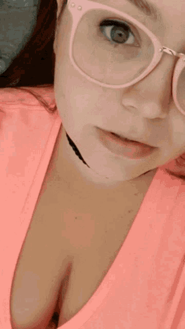 a woman wearing pink glasses and a choker is pointing at her chest