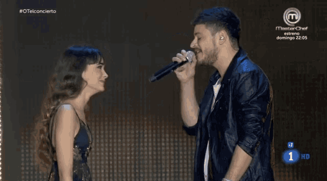 a man singing into a microphone next to a woman with the number 1 on the bottom left