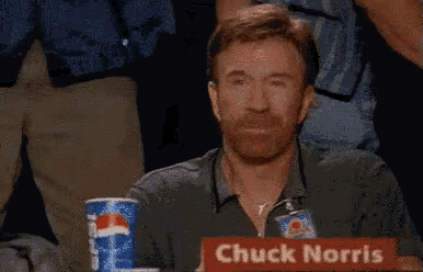 a man with a beard is sitting at a table with a sign that says chuck norris on it .