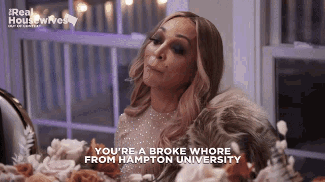 a woman sitting at a table with flowers says you 're a broke whore from hampton university